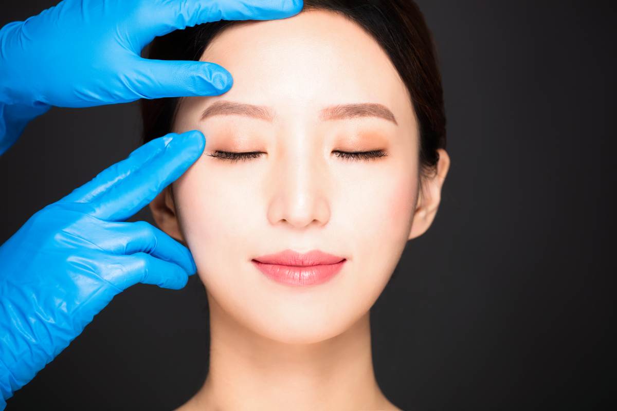 Surgeon examining woman’s eyelids before Asian double eyelid surgery to create a defined eyelid fold.